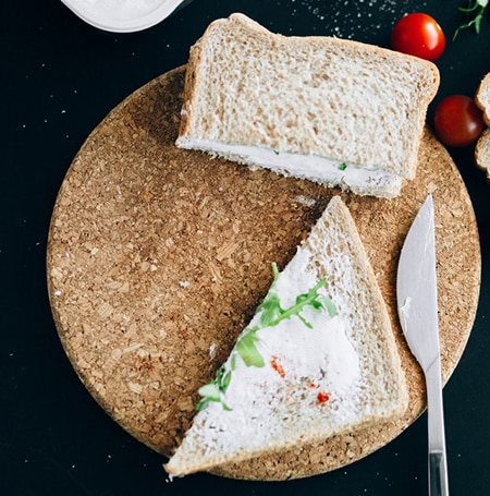 Un sandwich de pain de mie au fromage frais est posé sur une planche à découper. Il y a des tomates cerises autour.