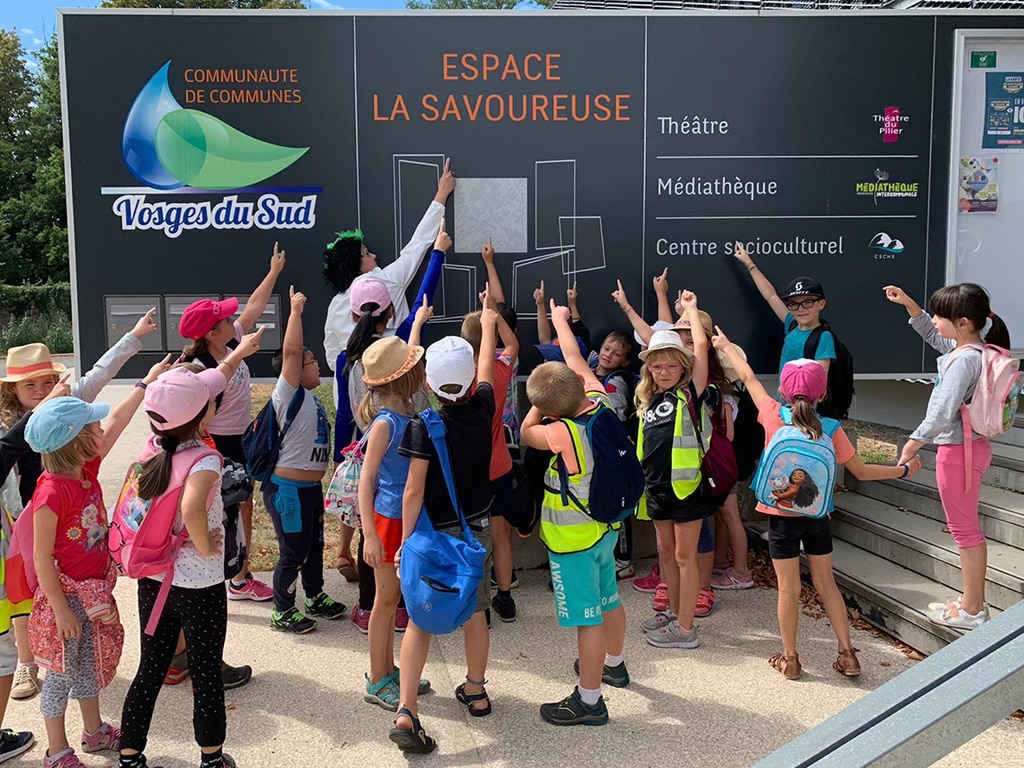 Des enfants pointent le doigt vers la pancarte d'accueil du Centre Socioculturel la Haute Savoureuse